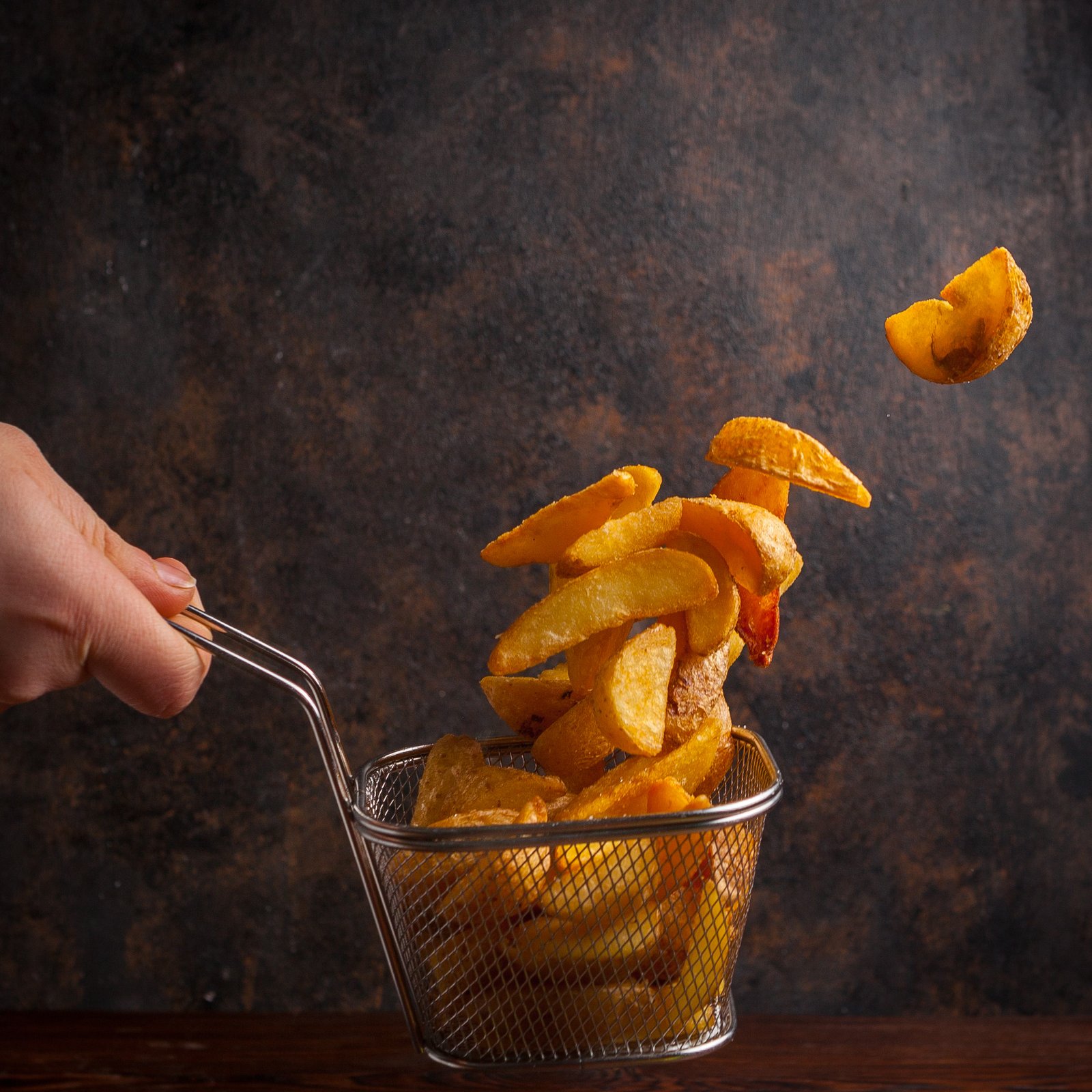 side-view-fried-potatoes-with-human-hand-in-grid-for-deep-frying.jpg